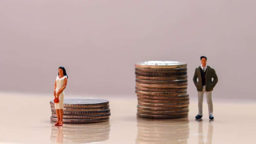 An illustration of gender discrimination, with a female in front of a small stack of coins and a male in front of a much larger stack of coins.