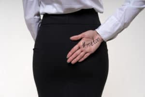 A woman has her hand behind her back with #MeToo written on her palm, indicating she has been a victim of sexual assault.