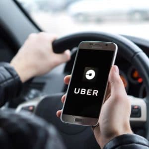 A driver is holding a phone with the Uber app showing on the phone screen.