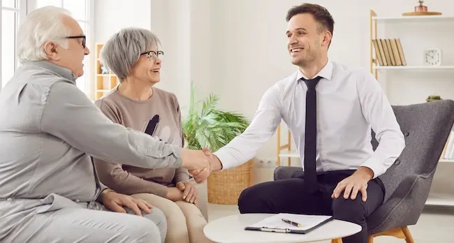 An injury lawyer is shaking hands with an elderly couple after explaining modified comparative fault rules and compensation recovery options.